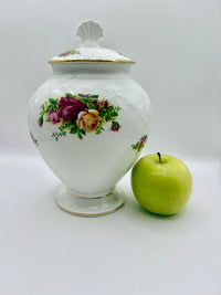 Decorative ceramic jar with floral design next to a green apple on a white background