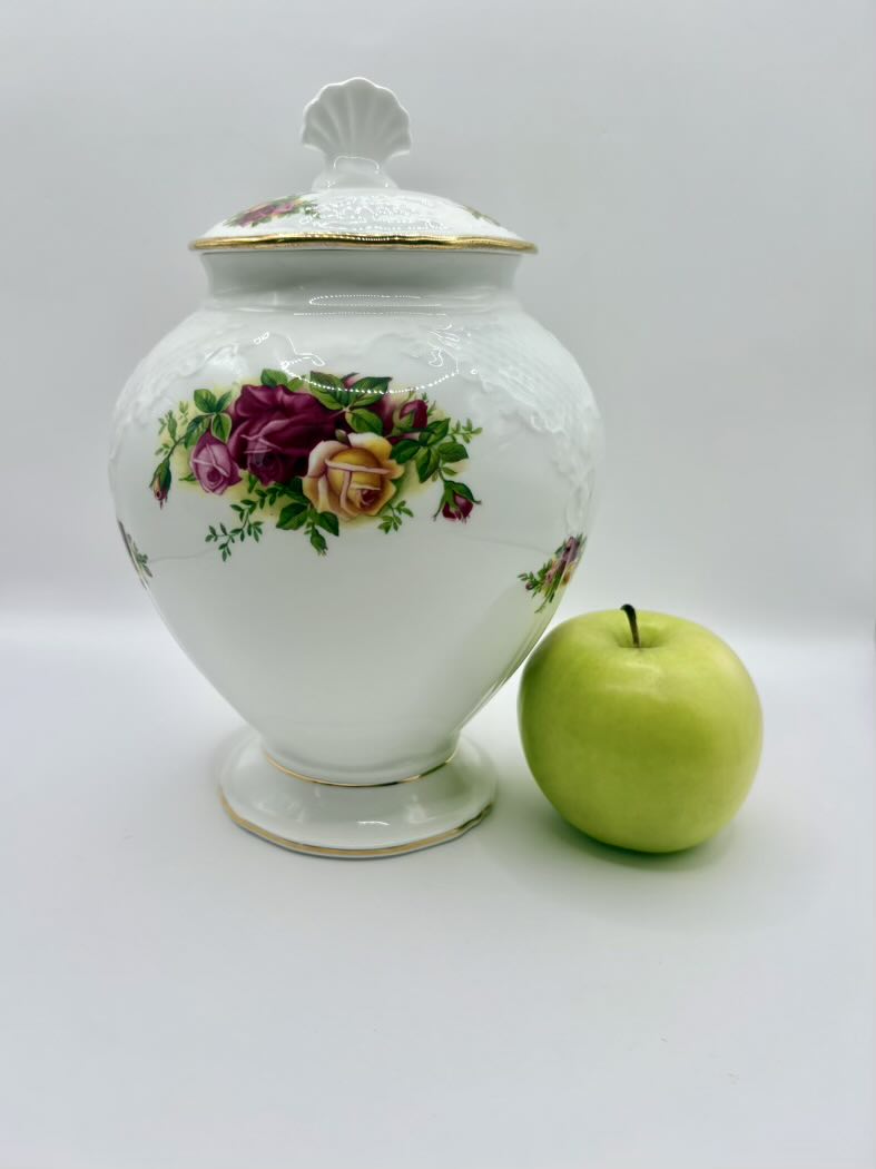 Decorative ceramic jar with floral design next to a green apple on a white background