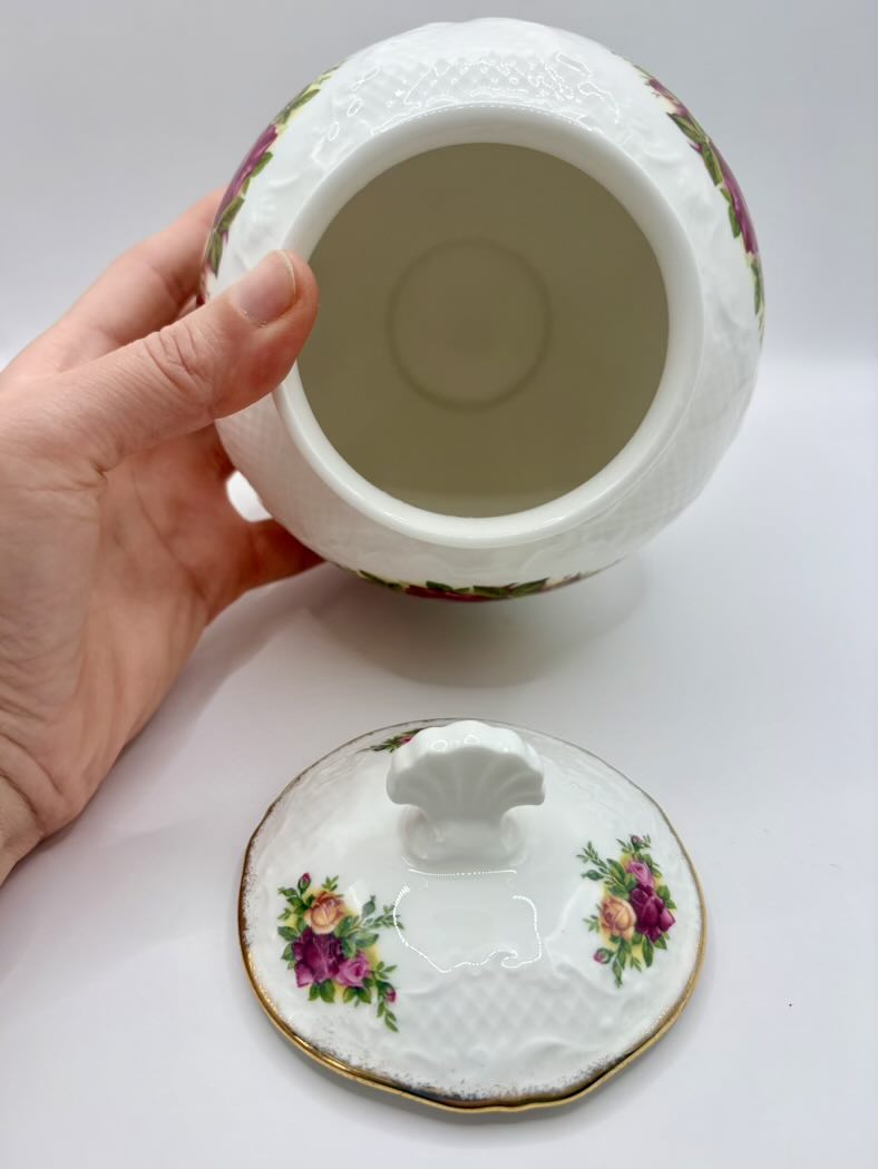 Decorative ceramic jar with lid held by a hand on a white background