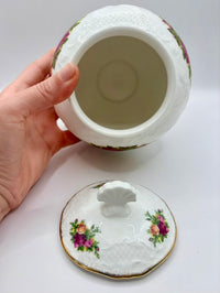 Decorative ceramic jar with lid held by a hand on a white background