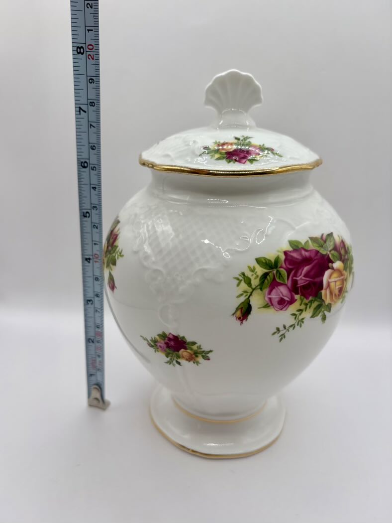 Decorative ceramic jar with floral designs and a measuring tape for scale on a white background