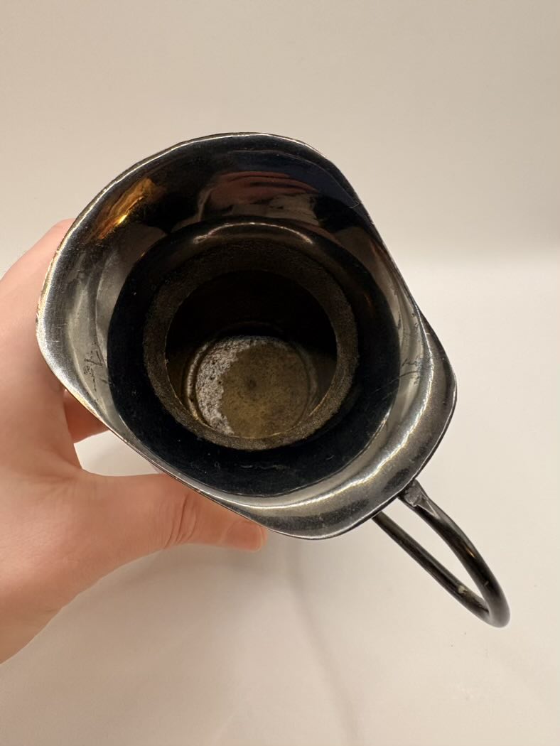 Hand holding a metal cup with a dark liquid against a plain background