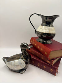 Decorative black and white ceramic duck and pitcher on a stack of books with a white background