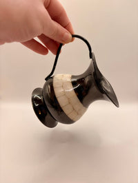 Black and white ceramic vase held by a hand against a plain background