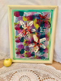 Colorful abstract painting with butterfly designs in a wooden frame on a lace tablecloth.