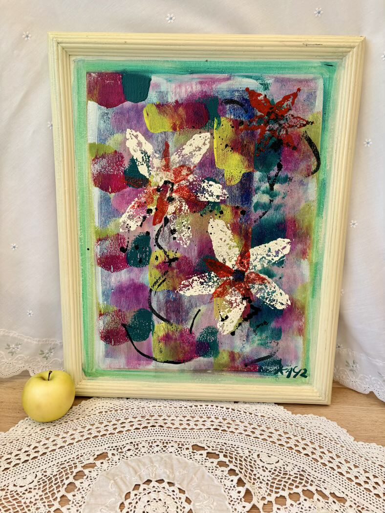 Colorful abstract painting with butterfly designs in a wooden frame on a lace tablecloth.