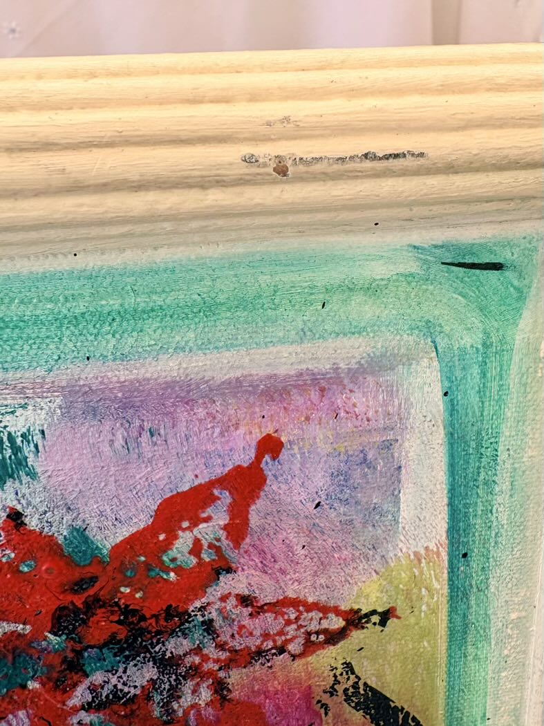 Close-up of a textured surface with colorful abstract art and wooden frame.