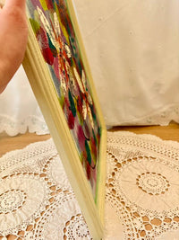 Colorful painting held by a hand on a lace tablecloth