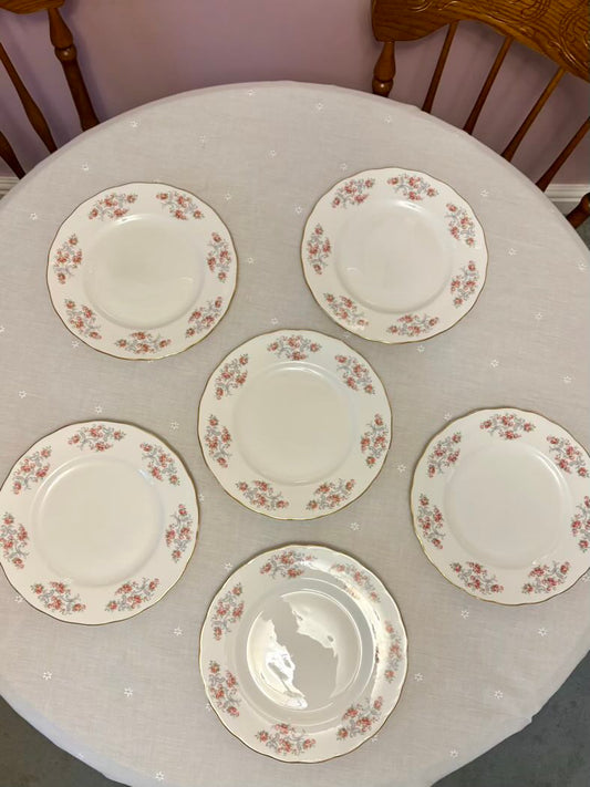 Set of six floral-patterned plates on a round table with a white tablecloth.