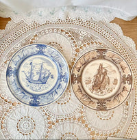 Two decorative plates with ship designs on a lace doily.