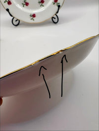 Close-up of a ceramic plate with a gold rim, showing a crack on the edge.
