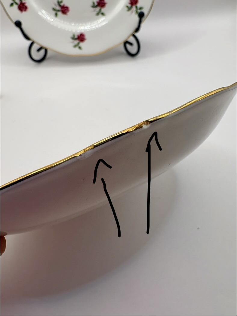 Close-up of a ceramic plate with a gold rim, showing a crack on the edge.