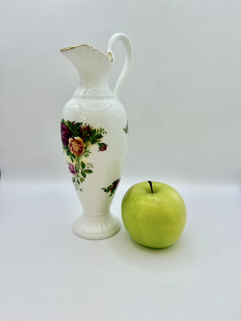 Decorative ceramic pitcher with floral design next to a green apple on a white background