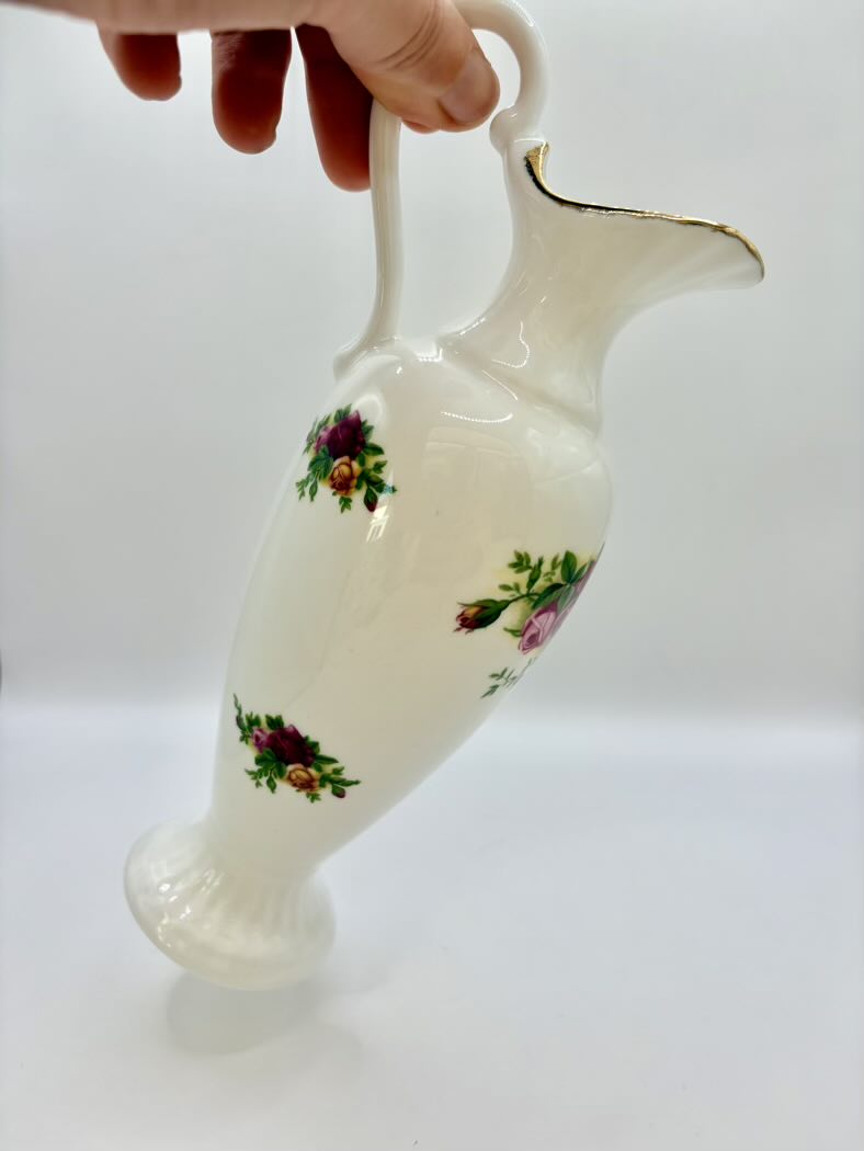 White ceramic pitcher with floral designs held by a hand on a white background