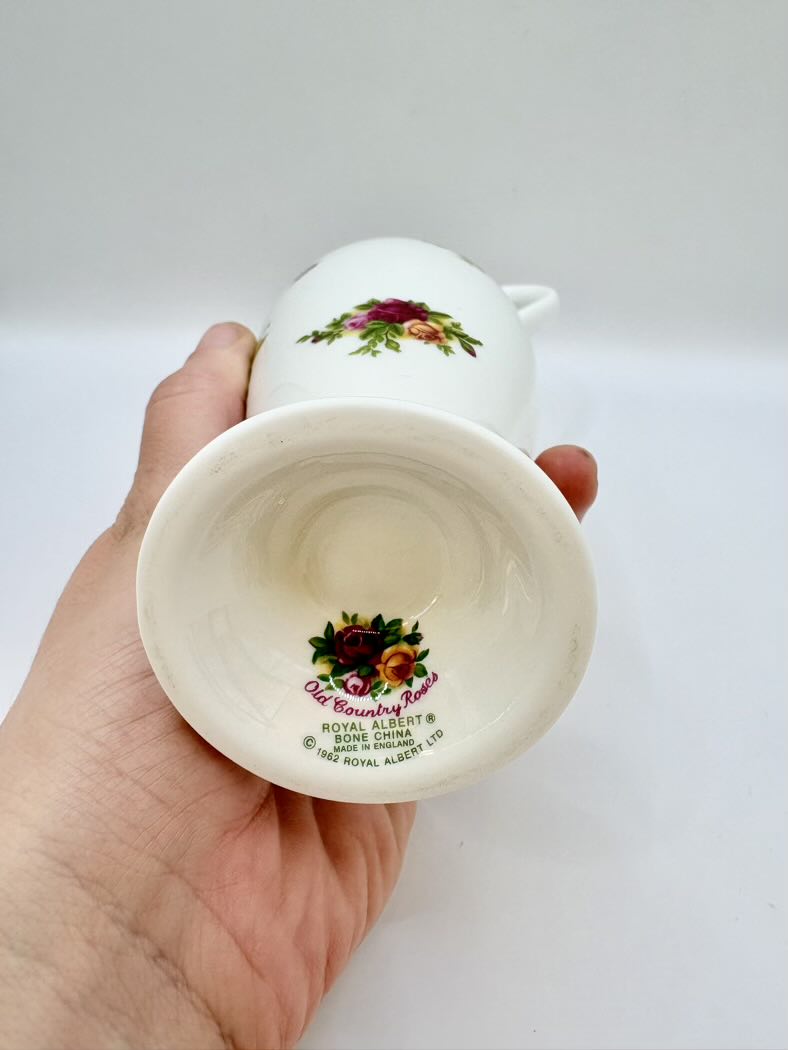 Hand holding a small white ceramic cup with floral design on a plain background