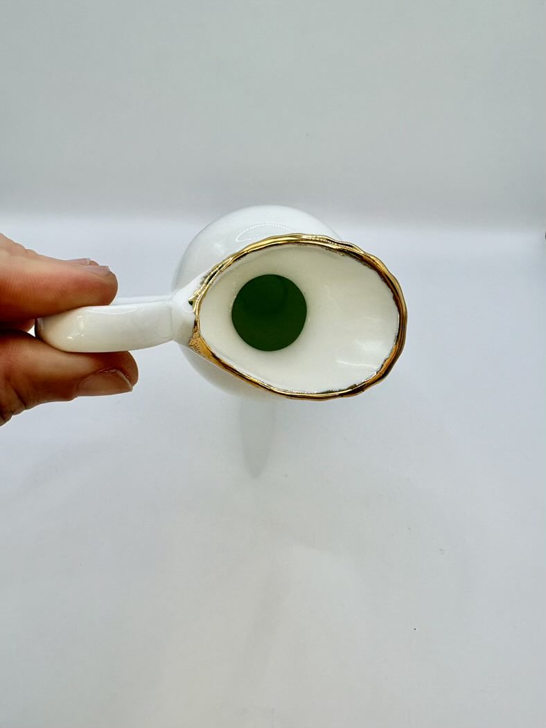 White ceramic spoon with gold rim held by a hand on a white background