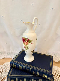 Decorative vase with floral design on a stack of blue books against a lace curtain background