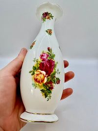 Decorative vase with floral design held by a hand against a plain background