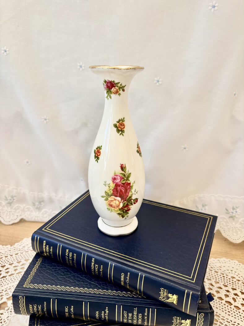 Decorative vase with floral patterns on a stack of blue books against a white lace curtain background
