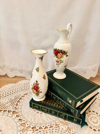 Two floral-patterned vases on top of green books with a lace tablecloth background
