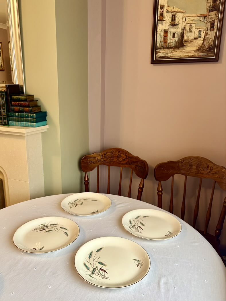 Dining table with four ceramic plates and two wooden chairs in a room with striped wallpaper and a framed picture on the wall.