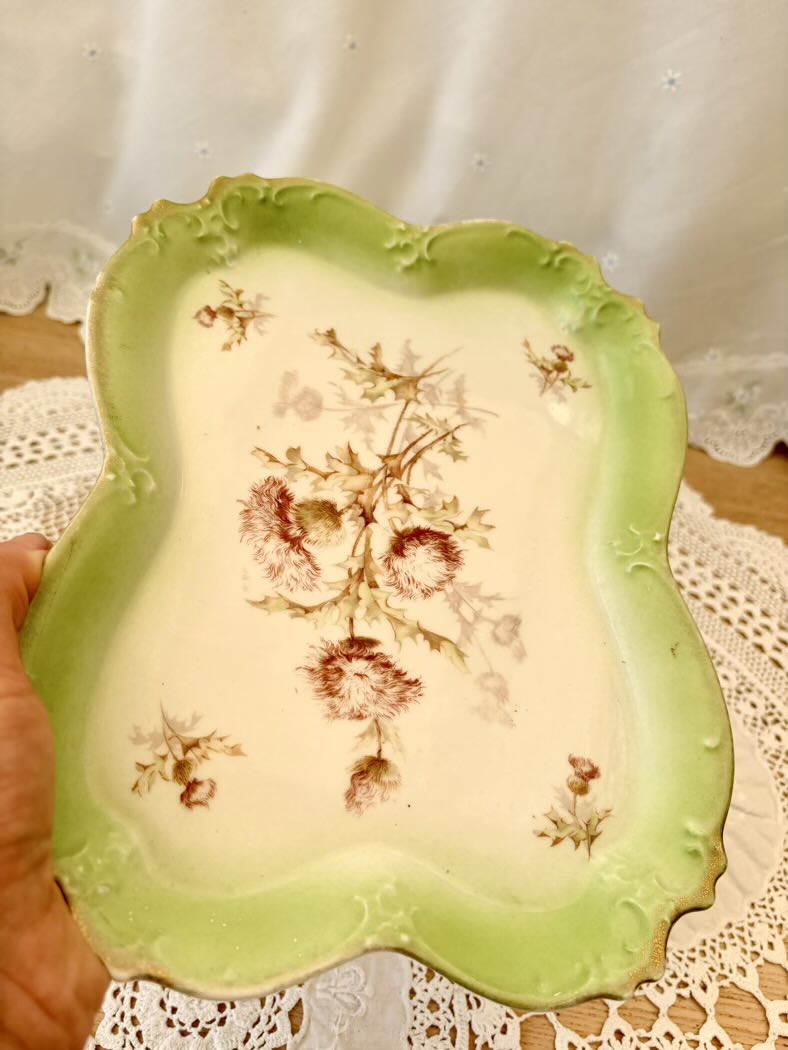 Decorative ceramic plate with floral design held by a hand on a lace tablecloth.