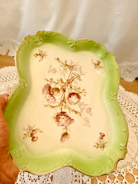 Decorative ceramic plate with floral design held by a hand on a lace tablecloth.