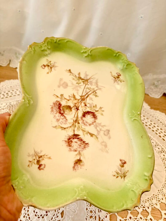 Decorative ceramic plate with floral design held by a hand on a lace tablecloth.