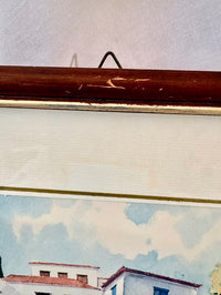 Framed artwork of a coastal scene with houses and clouds.