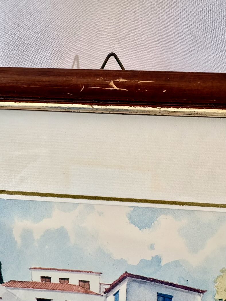 Framed artwork of a coastal scene with houses and clouds.