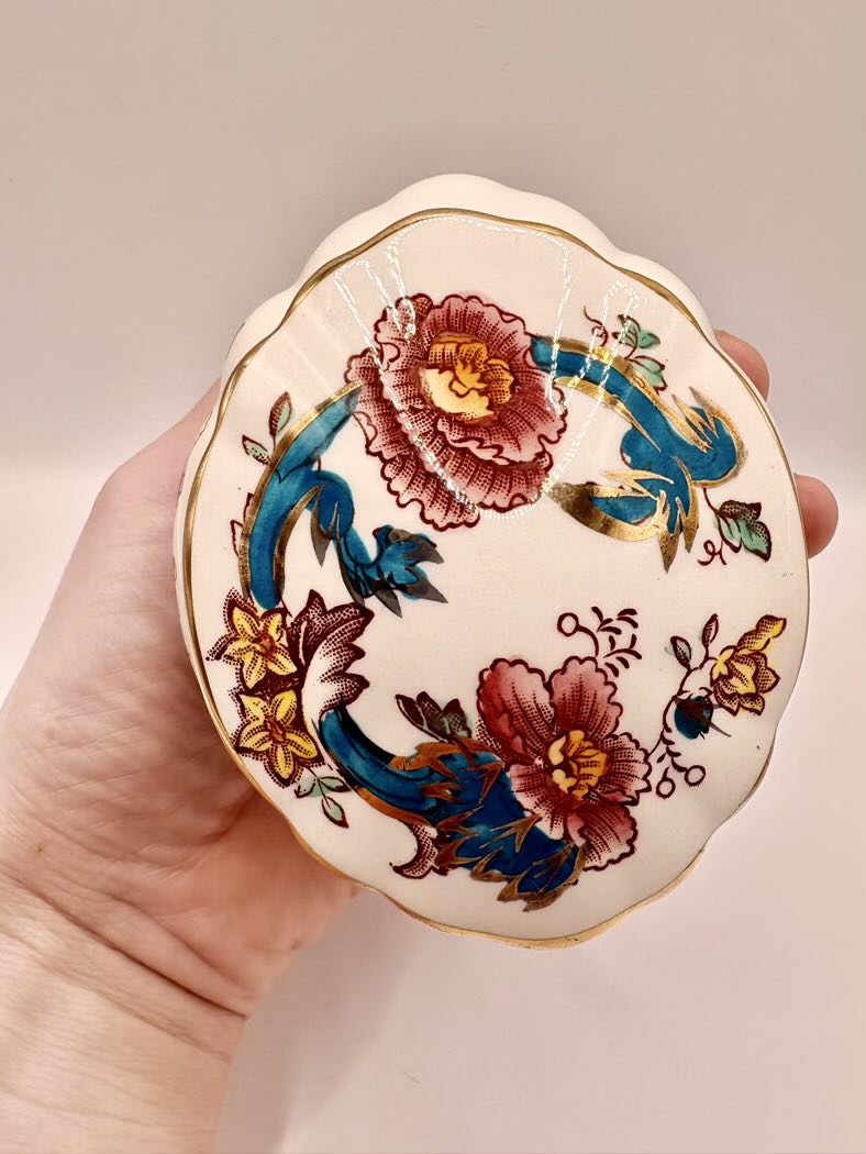 Decorative trinket box with floral designs held in a hand against a neutral background