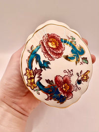 Decorative trinket box with floral designs held in a hand against a neutral background
