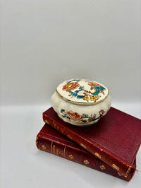 Decorative ceramic box with floral design on top of two red books against a gray background