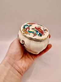 Hand holding a decorative ceramic container with floral designs on a plain background