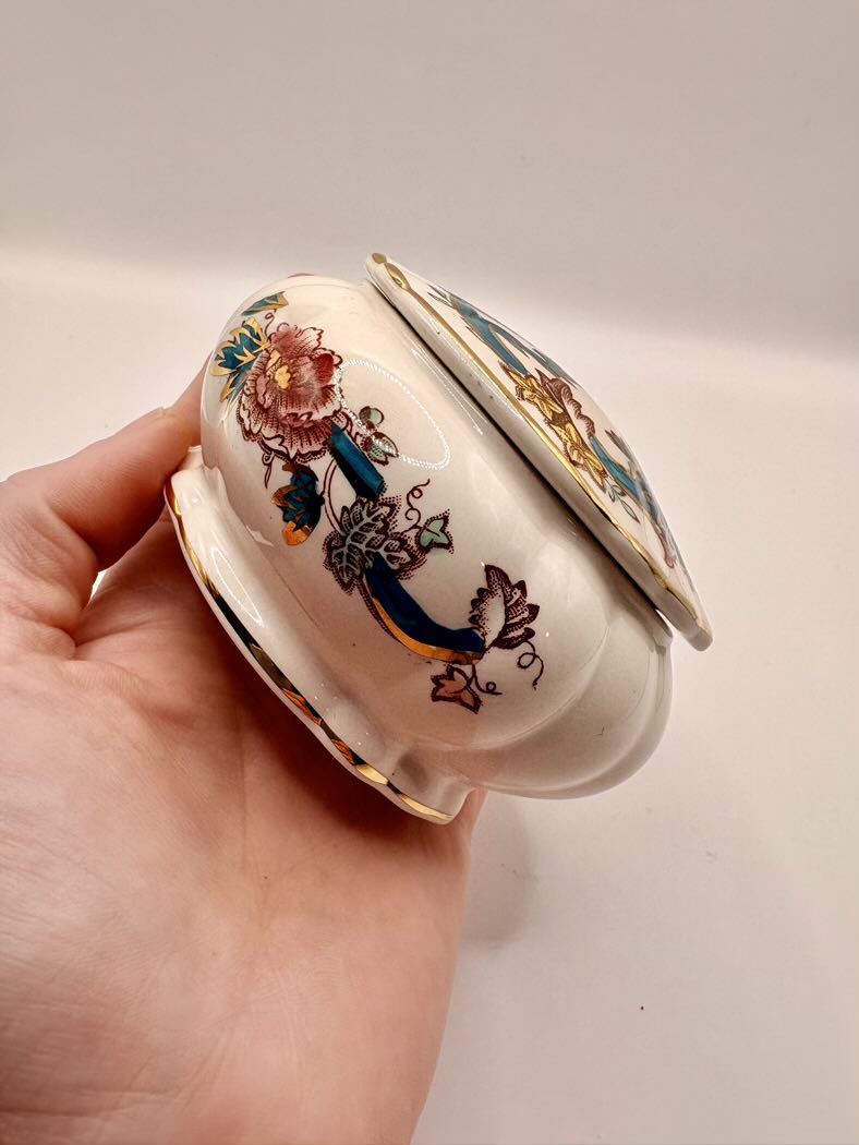 Hand holding a decorative ceramic container with floral designs on a plain background