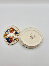 Decorative ceramic box with floral design on lid and text on base against a white background