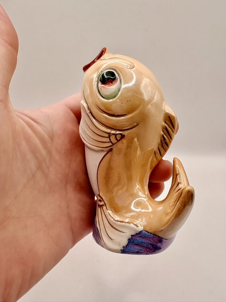 Hand holding a ceramic fish-shaped object against a plain background