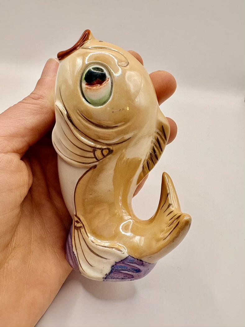 Hand holding a ceramic fish-shaped object with a white background