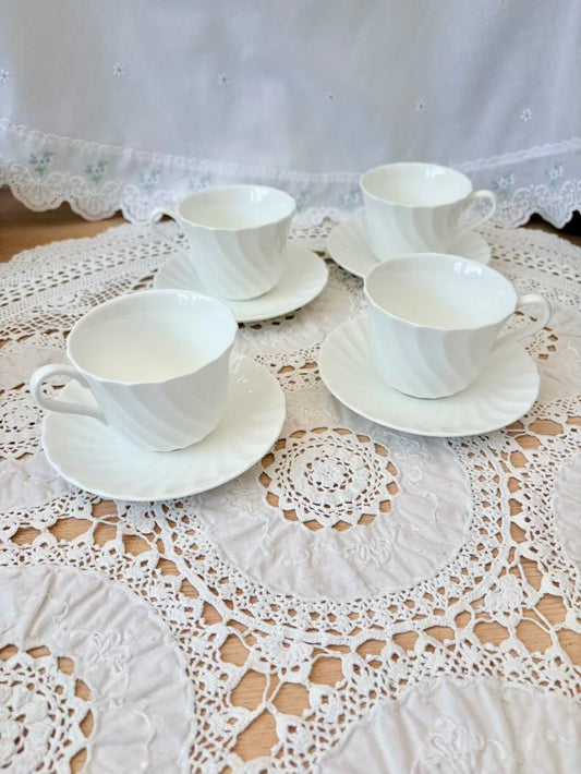 Set of four white teacups and saucers on a lace tablecloth