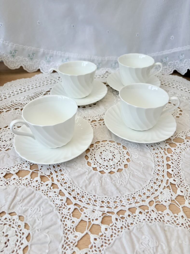 Set of four white teacups and saucers on a lace tablecloth