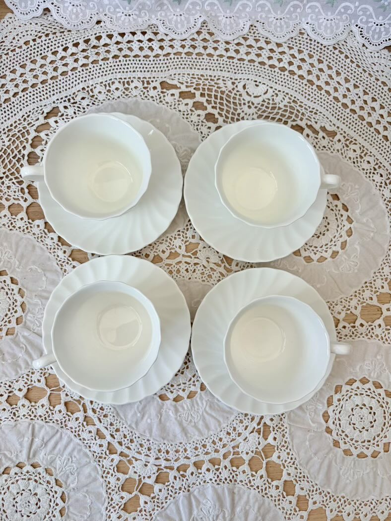 Four white teacups and saucers on a lace tablecloth
