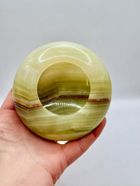 Hand holding a green stone with concentric circles against a white background
