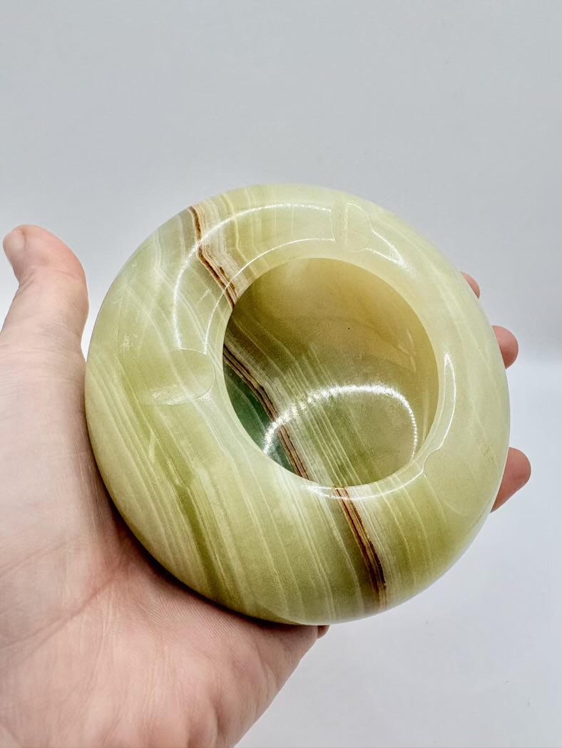 Hand holding a green stone with brown stripes against a plain background