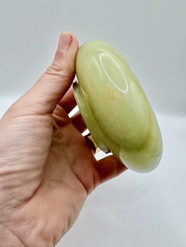 Hand holding a light green stone against a plain background