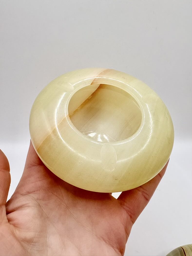 Hand holding a yellowish-brown stone with a central hole against a white background