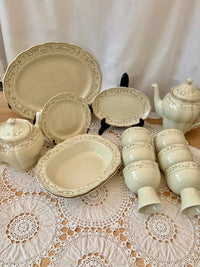 Set of ceramic dishes including teapots, plates, and bowls on a lace tablecloth.