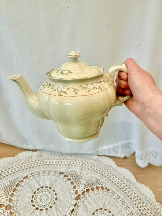 Hand holding a decorative ceramic teapot on a lace tablecloth