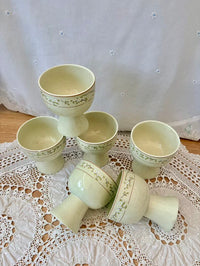 Set of ceramic egg cups on a lace tablecloth with a white curtain background