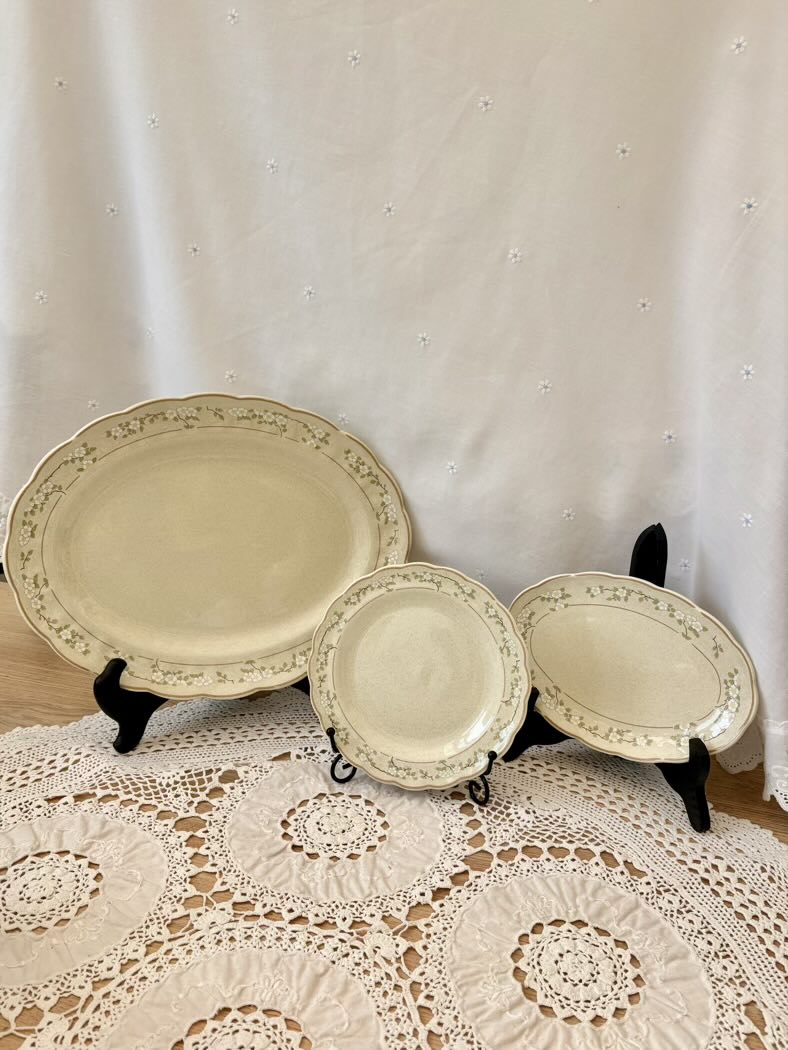 Set of three decorative plates on stands against a white curtain background