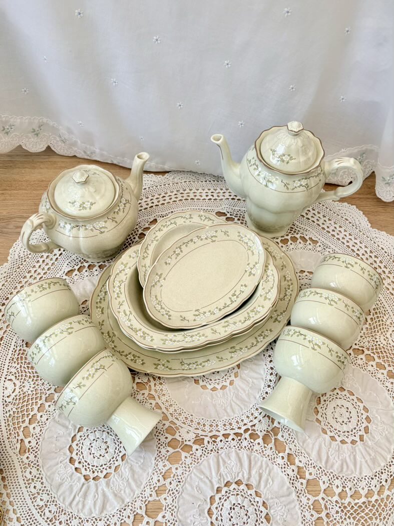 Ceramic tea set with teapot, cups, and plates on a lace tablecloth.